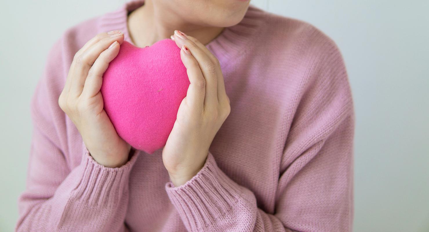 A woman holds a red heart-shaped pillow to her chest, symbolising heart health.