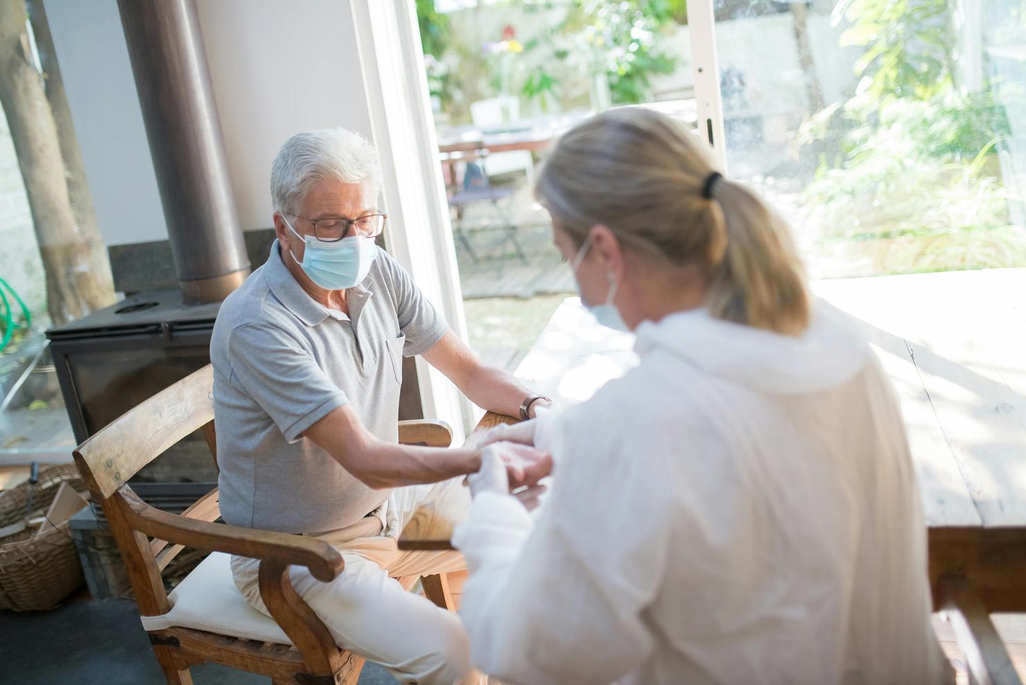 A home visiting practitioner takes a pulse reading from an older person in preparation for an immunisation.