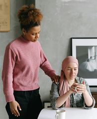 A female places her hand on the shoulder of another person, who is sitting in a chair