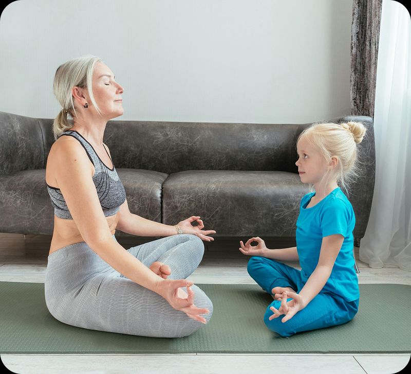 An older lady practices yoga on a yoga mat with her grand daughter