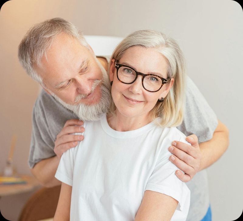 An older couple embrace each other, smiling and looking at the camera
